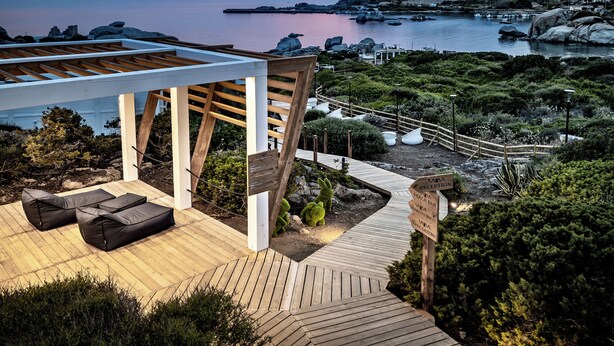 Een houten terras met buitenmeubelen, een receptie en uitzicht op de zee en een rotsachtig landschap.