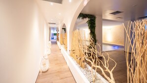 Een gang met houten vloer, witte wanden en decoratieve details, waaronder planten en wandpanelen met structuur.