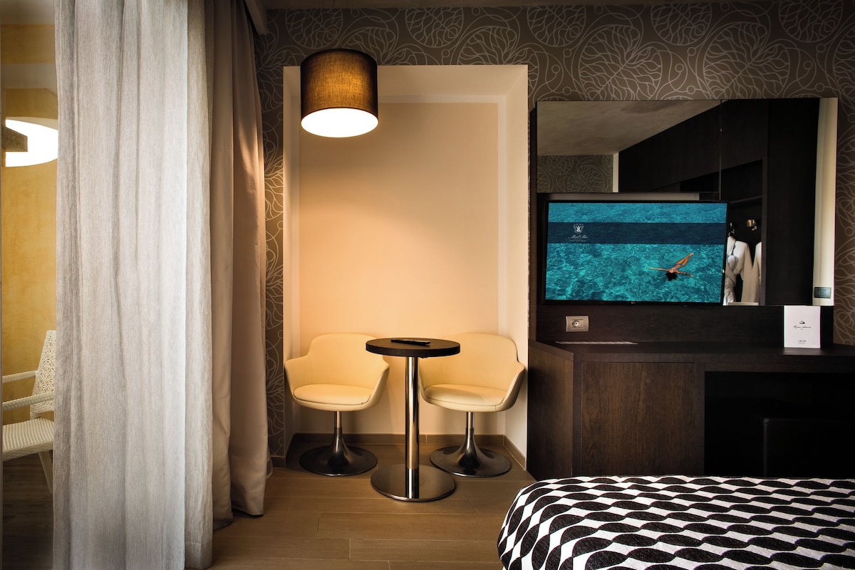 Een hotelkamer met een bed, een televisie, twee stoelen, een tafeltje en een spiegel.