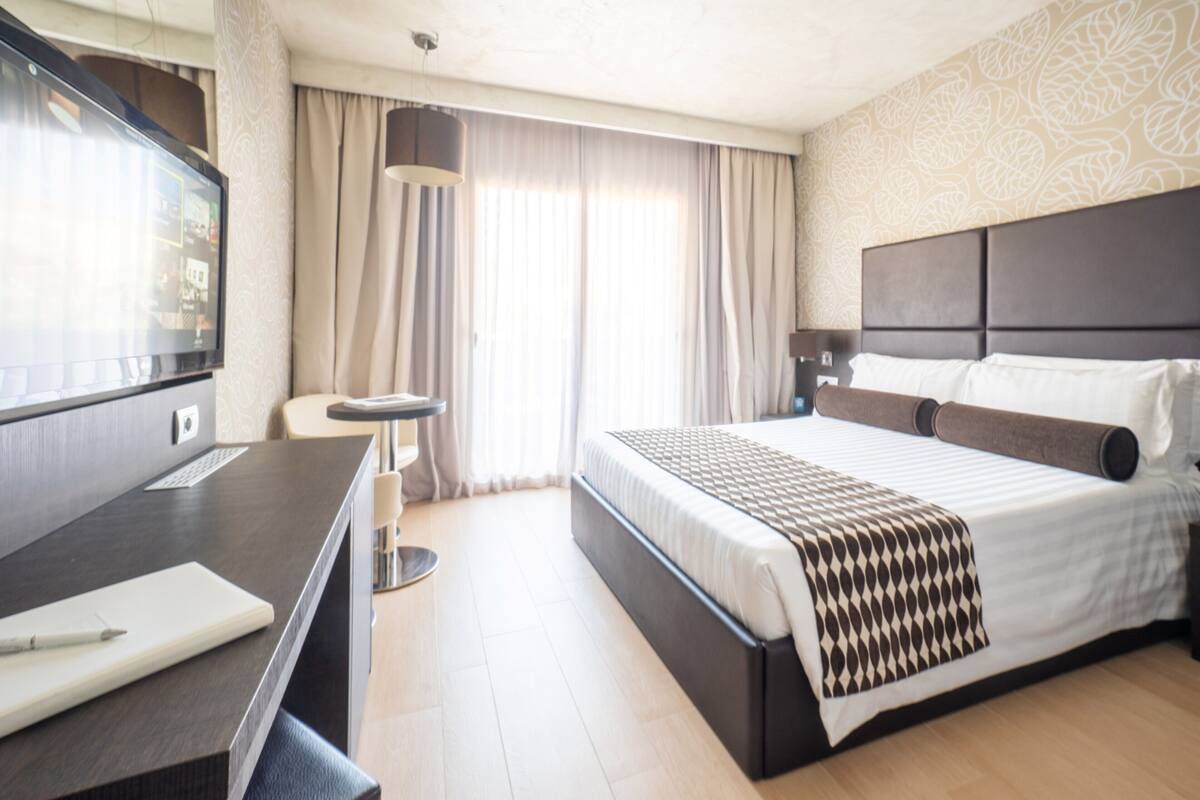 A hotel room with a bed, a desk, a chair, a TV, and curtains.