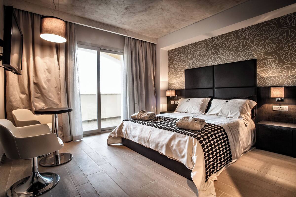 A modern hotel room with a large bed, a sitting area, and a view of the outdoors.