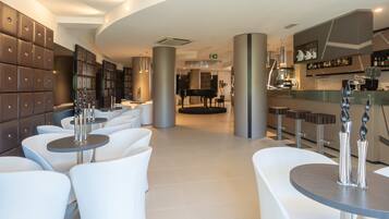 A modern hotel lobby with white seating, a bar area, and a grand piano.