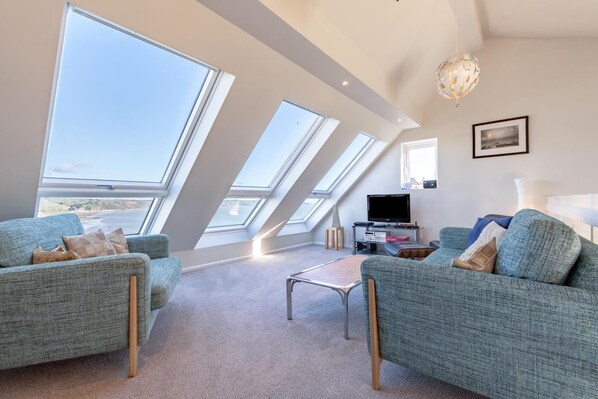 Un salon moderne doté d’une grande fenêtre offrant une vue panoramique, d’un téléviseur à écran plat et d’un coin salon confortable.