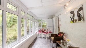 Ein sonnendurchflutetes Zimmer mit einem Esstisch, Stühlen, großen Fenstern und Korbmöbeln.