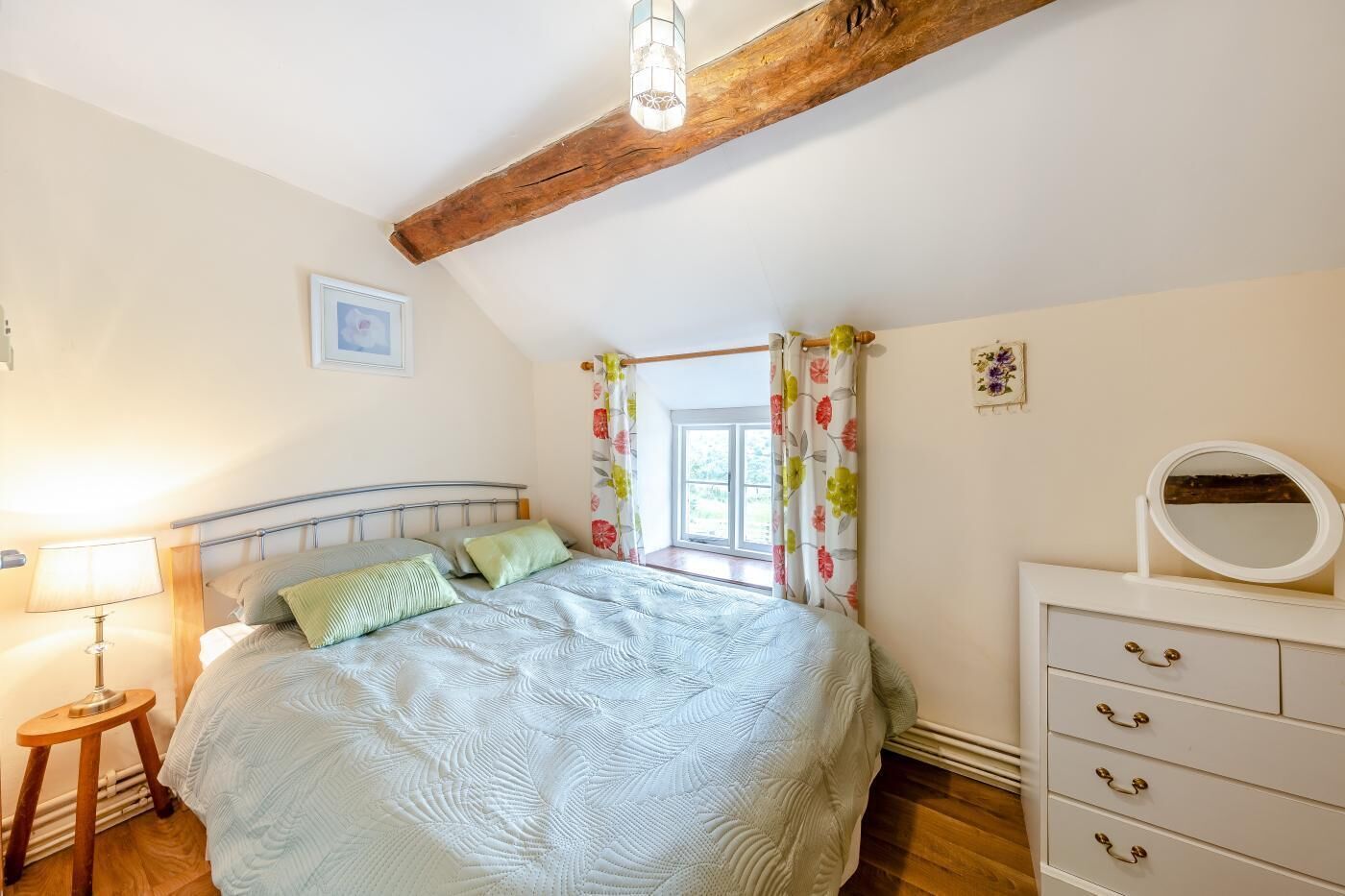 Ein Schlafzimmer mit einem Bett, einem Schminktisch, einer Lampe und einem Fenster mit Vorhängen.