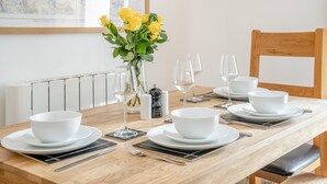 Een eettafel gedekt met witte kommen, wijnglazen en een vaas met gele bloemen.