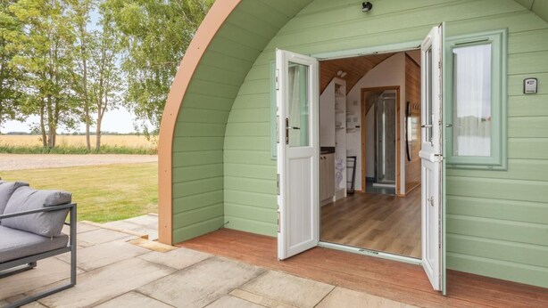 A cozy, single-room cabin with a wooden floor, a small kitchen area, and a door leading to a porch with a chair.