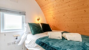 A bedroom with a curved wooden ceiling, a bed with white and teal bedding, two pillows, and a wall-mounted light.