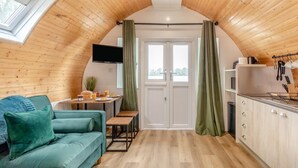 A cozy, semi-open living and dining area with a wooden ceiling, a teal sofa, a dining table with breakfast items, and a kitchen with a sink and utensils.