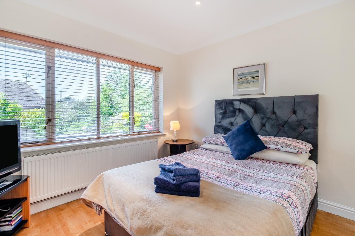 Een slaapkamer met een bed, nachtkastje met lamp, raam met zonwering en radiator.