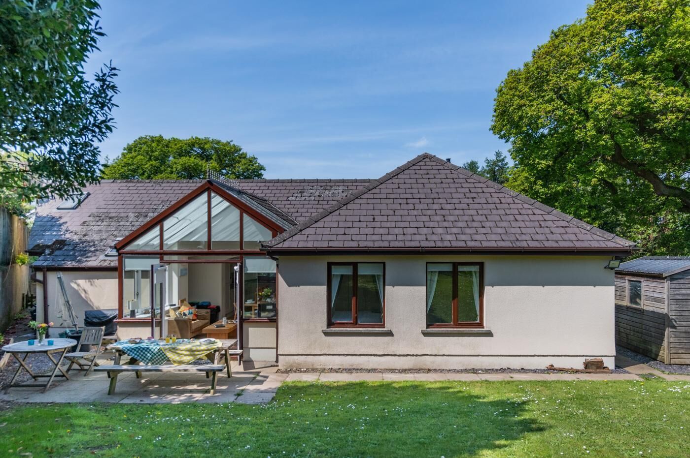 Ein Bungalow mit geneigtem Dach, Glastür und kleiner Terrasse mit Tisch und Stühlen.