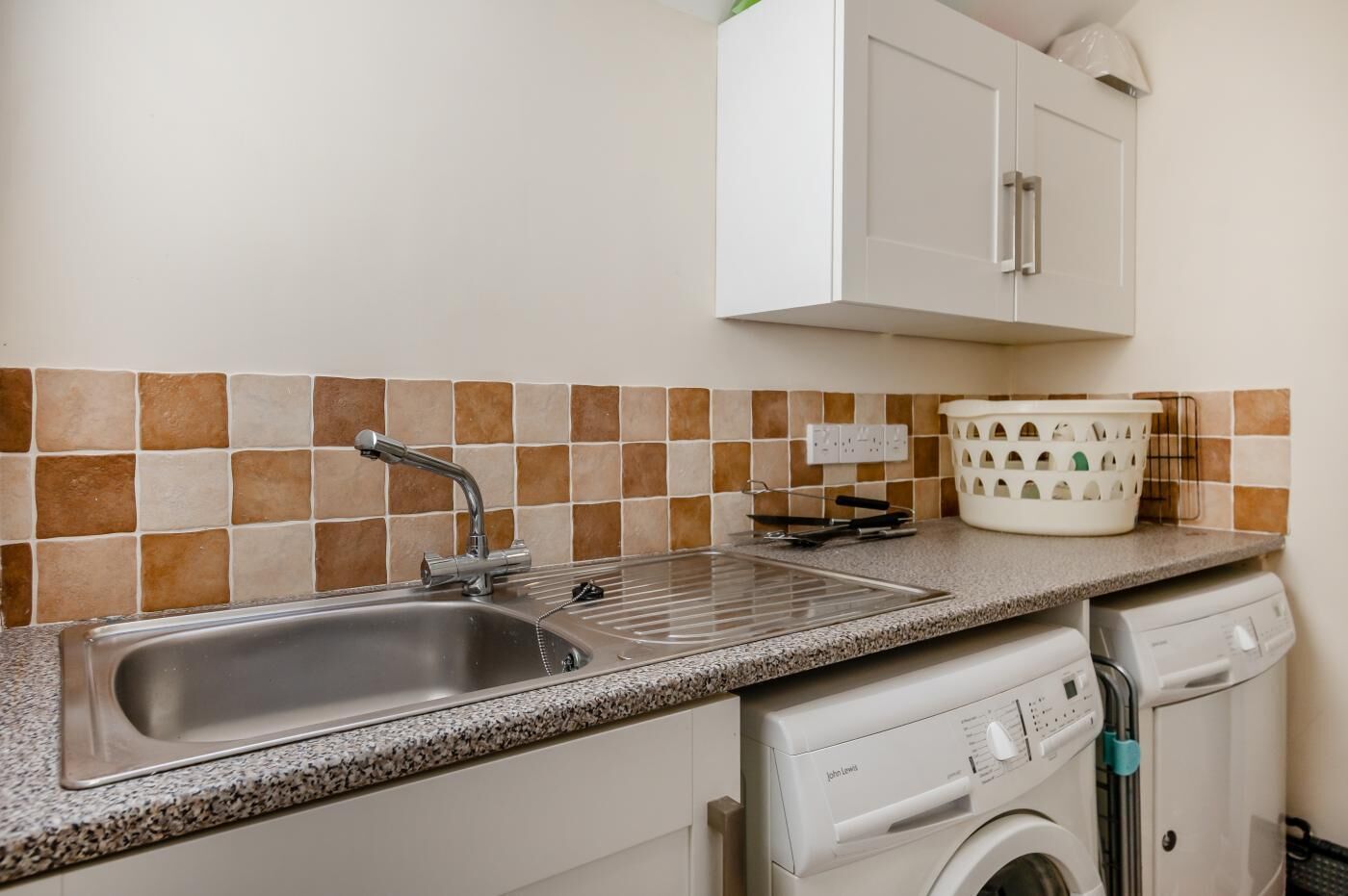 A kitchen with a double sink, a dish rack, a washing machine, and a cabinet above the sink.