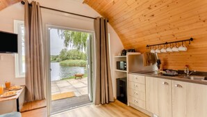 A compact kitchen with a view of a river, wooden ceiling, and a sliding door leading to an outdoor area.