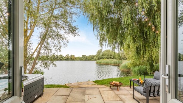 An outdoor patio with a view of a lake, a seating area with a table and chairs, and a grill.