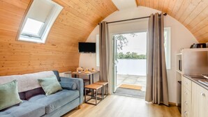 A cozy room with a wooden ceiling, a sofa, a small table with a TV, and a view through a door.