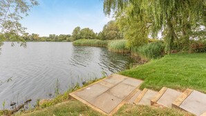 A riverside walkway with a concrete platform leading into the water, surrounded by lush greenery and trees.