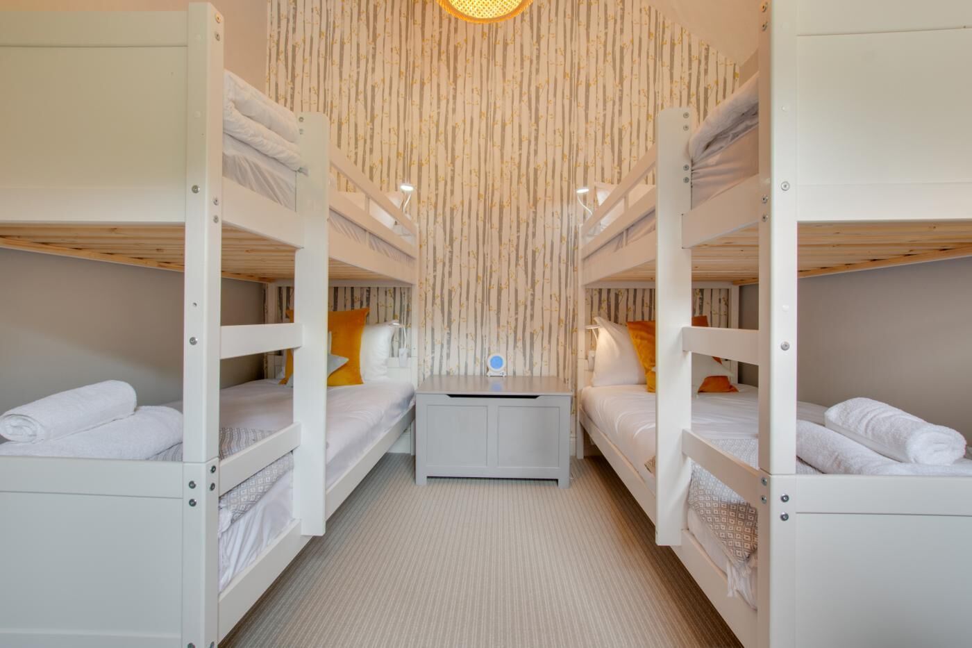 A bunk bed room with two beds, a desk, and a hanging light fixture.