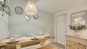 Un comedor con una mesa de madera dispuesta para seis personas, una lámpara colgante y una puerta blanca con ventana.