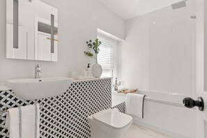 A modern bathroom with a white sink, mirror, and shower. There is a patterned wall and a small plant on the vanity. - 2 Bed in Saundersfoot (oc-pw252a) (Saundersfoot)