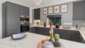 A modern kitchen with dark grey cabinets, a marble countertop, and a built-in oven. There are framed artworks on the wall, a potted plant, and a variety of fruits and vegetables on the counter. - 2 Bed in Saundersfoot (oc-pw252a) (Saundersfoot)
