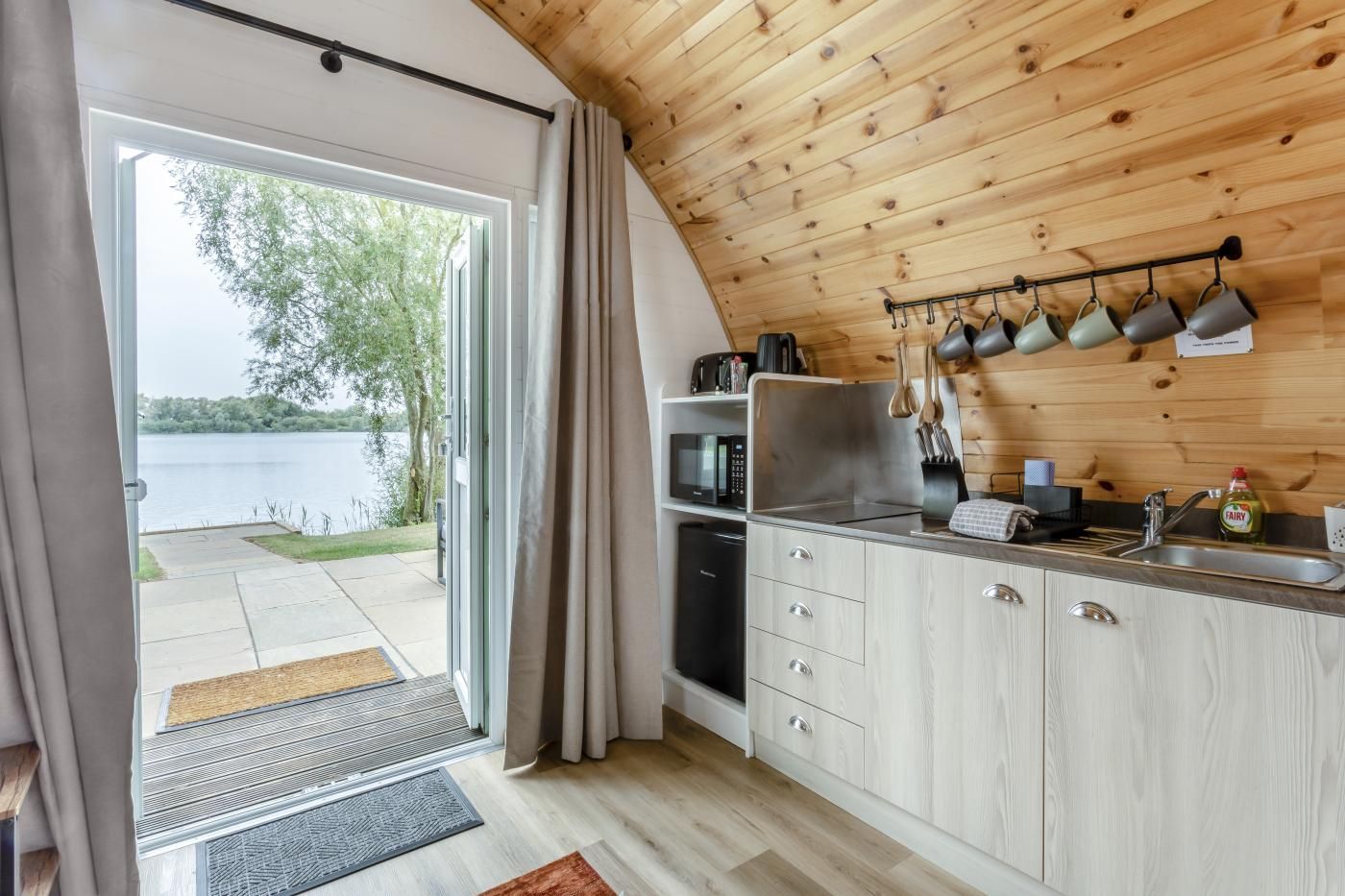 Een keuken met uitzicht op een meer, een houten plafond en een schuifdeur naar buiten.