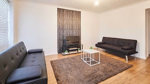 A modern living room with a black sofa, a white coffee table, and a TV stand. - Host & Stay | Coquet House (Ellington)