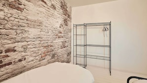 A room with a brick wall, a metal shelving unit, and a bed with white bedding. - Host & Stay | Coquet House (Ellington)
