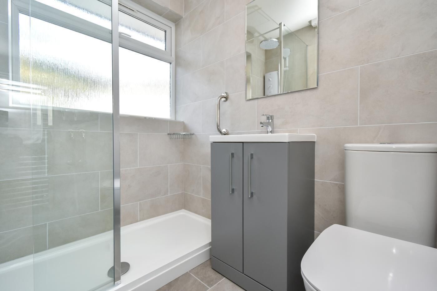 A bathroom with a glass-enclosed shower, a sink with a mirror, and a toilet.