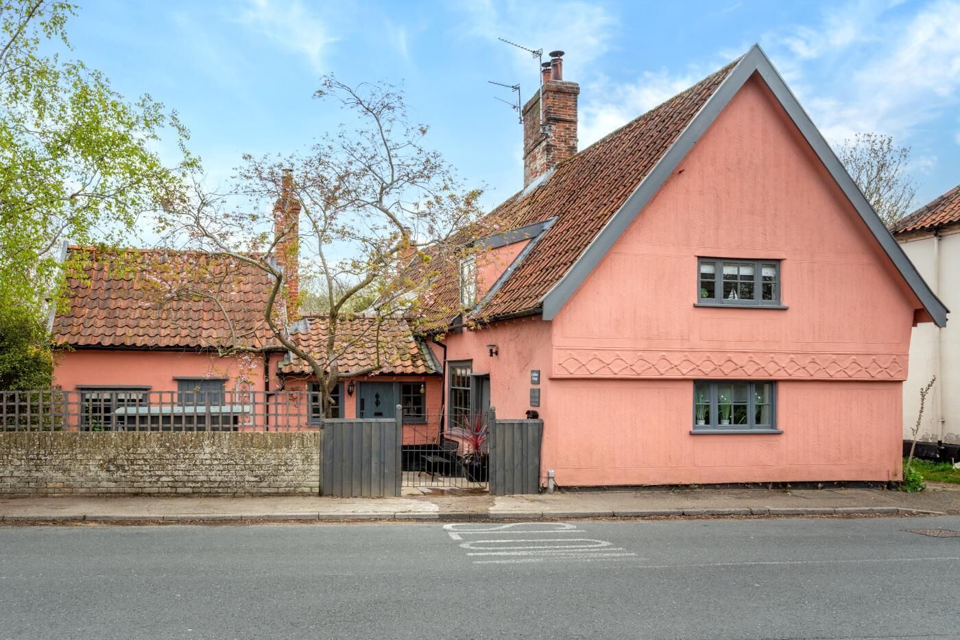 Une maison rose avec un toit en tuiles et une cheminée, une allée bordée de portails et un ciel dégagé.