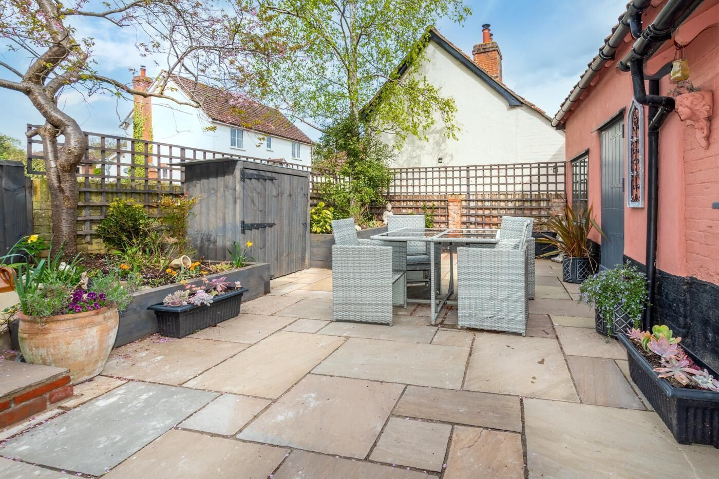 A patio with a table and chairs, surrounded by potted plants and a wooden fence.