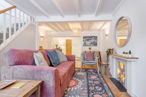 Ein gemütliches Wohnzimmer mit einem gestreiften Sofa, einem Couchtisch aus Holz, einem gemusterten Teppich, einem Kamin und einer Treppe, die in einen anderen Raum führt.