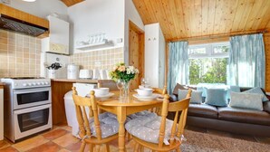Une cuisine chaleureuse avec une table à manger, des chaises et un canapé dans un coin salon offrant une vue sur la verdure.