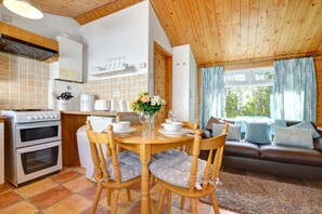 Une cuisine chaleureuse avec une table à manger, des chaises et un canapé dans un coin salon offrant une vue sur la verdure.
