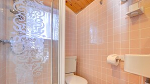 Une salle de bain avec des carreaux roses, des toilettes, une douche avec une porte en verre et un rouleau de papier toilette accroché au mur.