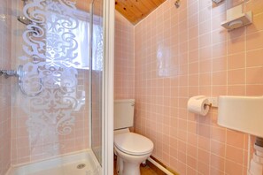 Une salle de bain avec des carreaux roses, des toilettes, une douche avec une porte en verre et un rouleau de papier toilette accroché au mur.