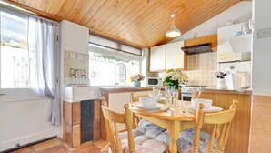 A cozy kitchen with wooden cabinets, a dining table set for four, and a window with curtains. - 2 Bed in Saundersfoot (oc-pw907a) (Saundersfoot)