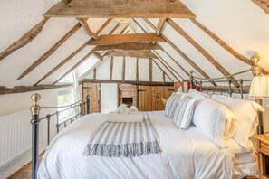 A bedroom with a high ceiling, exposed wooden beams, a brick fireplace, and a bed with white linens and striped pillows. - 2 Bed in Dedham (oc-c32543) (Dedham)