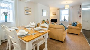 A dining area with a wooden table set for four, white chairs, and a sofa with cushions. - 2 Bed in Betws Y Coed (oc-wag474) (Betws-y-coed)