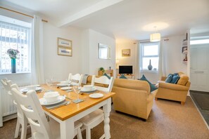 A dining area with a wooden table set for four, white chairs, and a sofa with cushions. - 2 Bed in Betws Y Coed (oc-wag474) (Betws-y-coed)