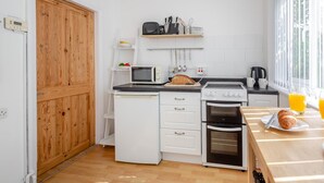 A compact kitchen with a microwave, toaster, oven, and a breakfast table with croissants and orange juice. - 2 Bed in Betws Y Coed (oc-wag474) (Betws-y-coed)