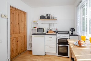 A compact kitchen with a microwave, toaster, oven, and a breakfast table with croissants and orange juice. - 2 Bed in Betws Y Coed (oc-wag474) (Betws-y-coed)