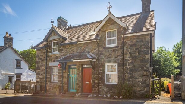 A stone building with a red door and a green door, two windows, and a chimney. - 2 Bed in Betws Y Coed (oc-wag474) (Betws-y-coed)