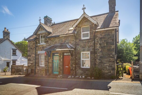 A stone building with a red door and a green door, two windows, and a chimney. - 2 Bed in Betws Y Coed (oc-wag474) (Betws-y-coed)