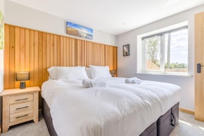 A bedroom with a large bed, wooden headboard, a nightstand with a lamp, a window with a view, and a painting on the wall.