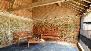 A covered outdoor seating area with wooden benches and a table, surrounded by a stone wall and a brick ceiling. - 3 Bed in Shereford (oc-2173) (Shereford)