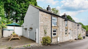 A stone house with a white exterior, a wooden table with a green umbrella, and a small garden area. - 2 Bed in Buxton (oc-dcwyn) (Tideswell)