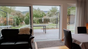 Een kamer met een schuifdeur die uitkomt op een terras buiten, met een tafel en stoelen.