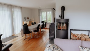 A modern living room with a fireplace, wooden flooring, a dining area with chairs and a table, and a sofa.