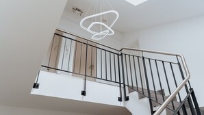 Een moderne trap met een metalen leuning, een witte muur en een bijzondere lamp.