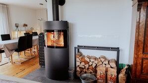 Een moderne woonkamer met een houtkachel, een eethoek en een stap houtblokken.